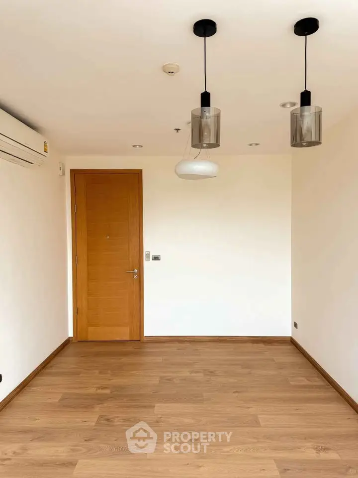 Spacious empty room with wooden flooring and modern lighting fixtures.