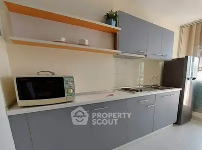 Modern kitchen with sleek cabinets, microwave, and fridge in a bright apartment.