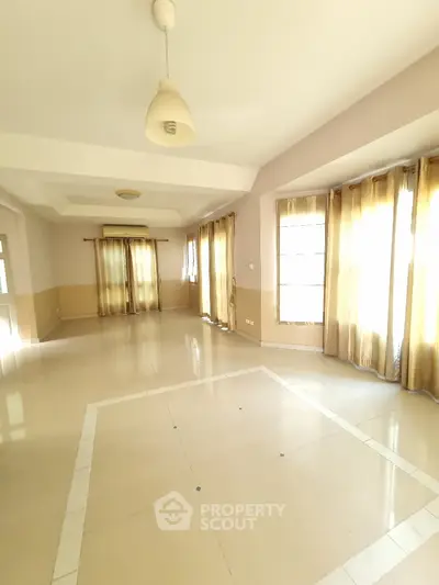 Spacious sunlit living room with elegant tile flooring and large windows