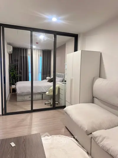 Modern apartment interior with cozy living room and stylish bedroom separated by glass doors.