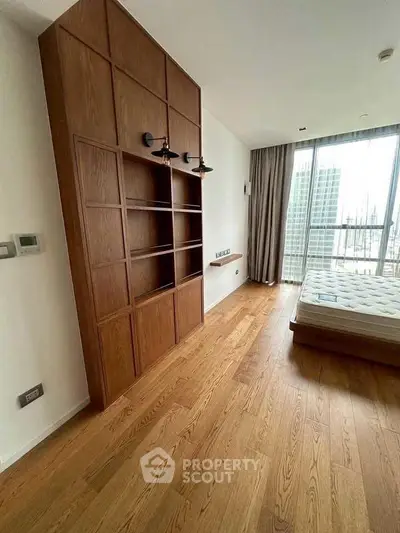 Spacious bedroom with wooden flooring and large window offering city views