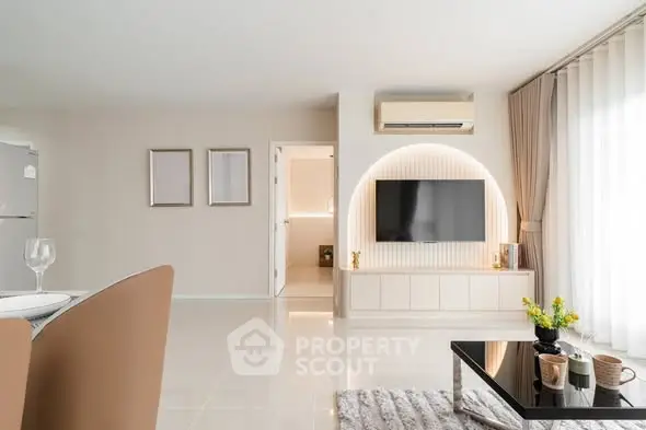 Modern living room with sleek decor, large TV, and natural light from floor-to-ceiling windows.