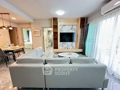Modern living room with sleek furniture and open layout, featuring a wall-mounted TV and large windows.
