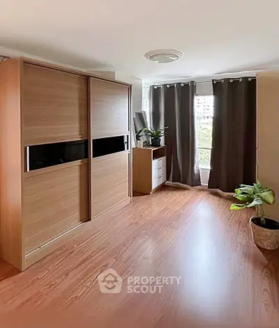 Spacious bedroom with wooden flooring and large wardrobe, featuring natural light from window.