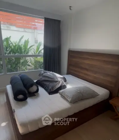 Cozy bedroom with large window and modern wooden bed frame, perfect for relaxation.