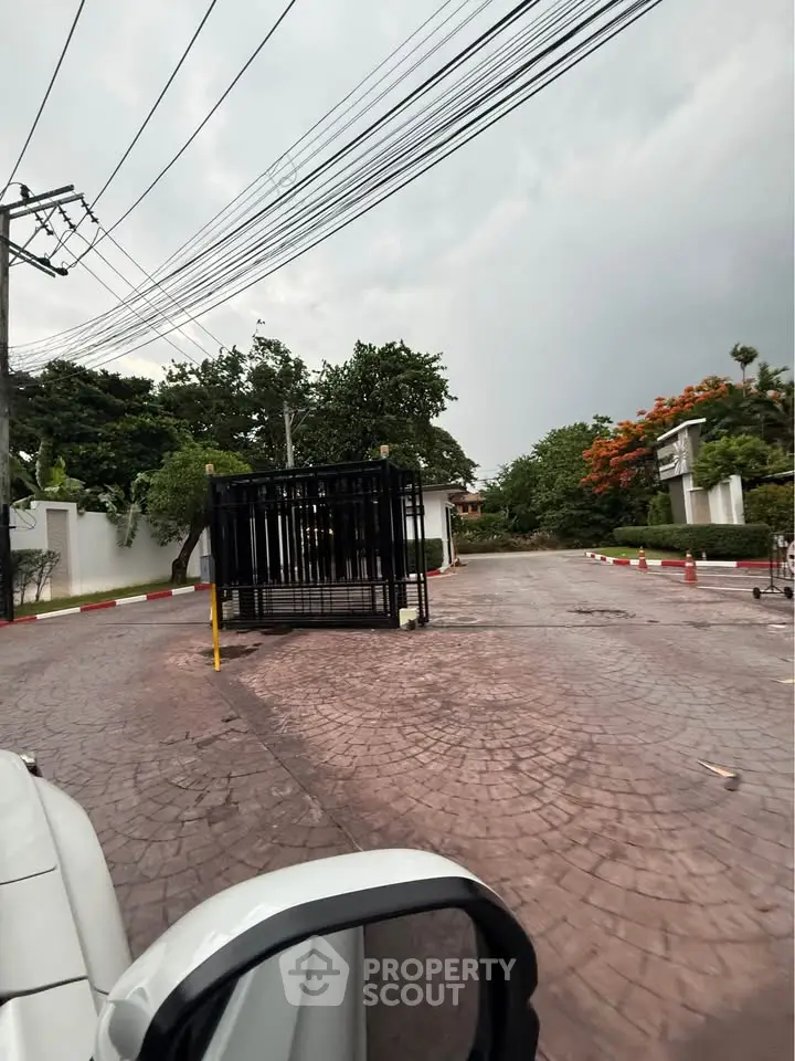 Secure gated entrance to a residential community with lush greenery and paved driveway.