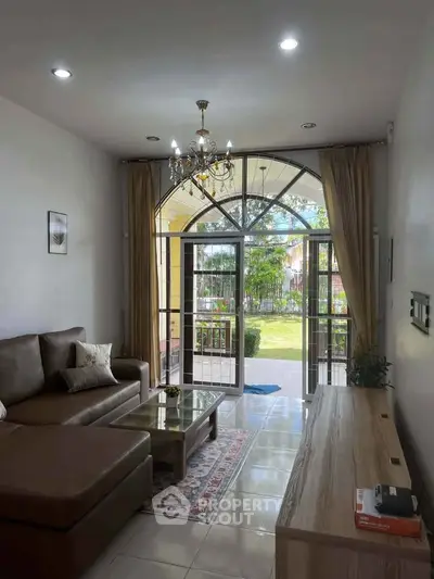 Elegant living room with chandelier and garden view, featuring a cozy sectional sofa and stylish decor.