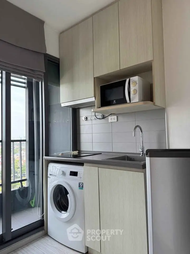 Modern compact kitchen with washing machine and microwave, featuring sleek cabinetry and balcony view.