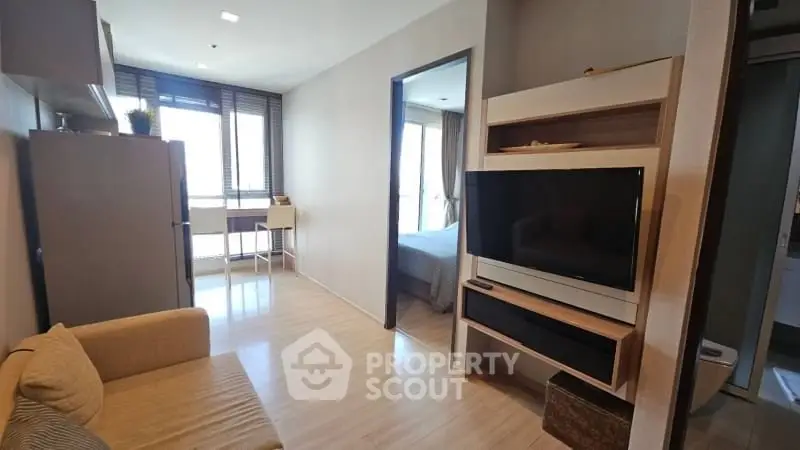 Modern living room with TV and cozy sofa, leading to a bright bedroom with large windows.