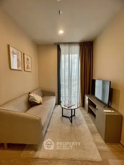 Cozy living room with modern sofa, TV, and natural light from large window.