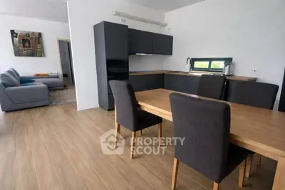 Modern open-plan kitchen and dining area with sleek dark cabinets and wooden table.