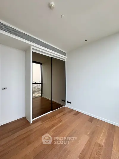 Spacious empty bedroom with wooden flooring and mirrored closet doors in modern apartment.