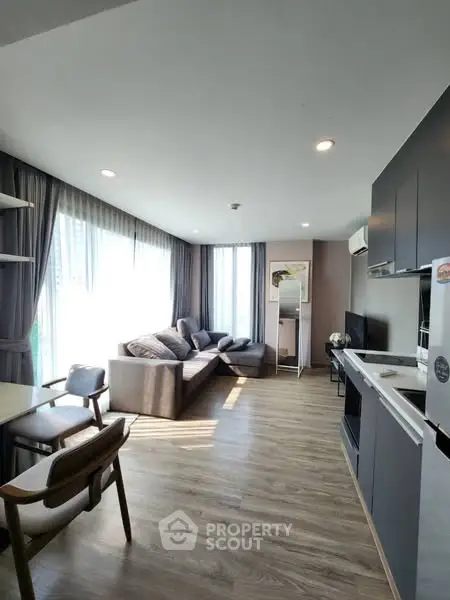 Modern living room with sleek kitchen, large windows, and stylish furniture in a bright apartment.