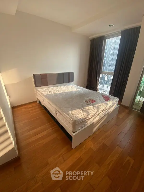 Spacious bedroom with wooden flooring and large window for natural light