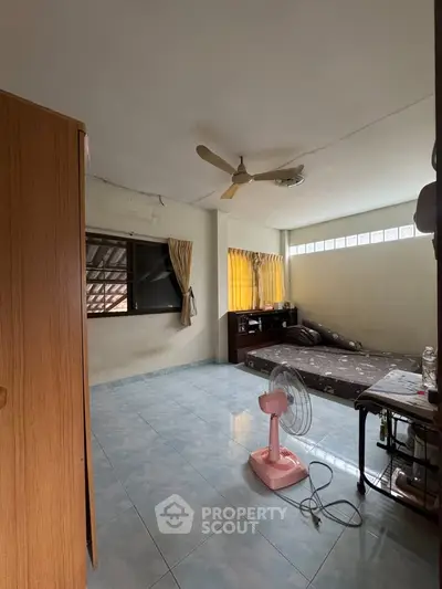 Spacious bedroom with natural light, ceiling fan, and tiled flooring, ideal for comfortable living.