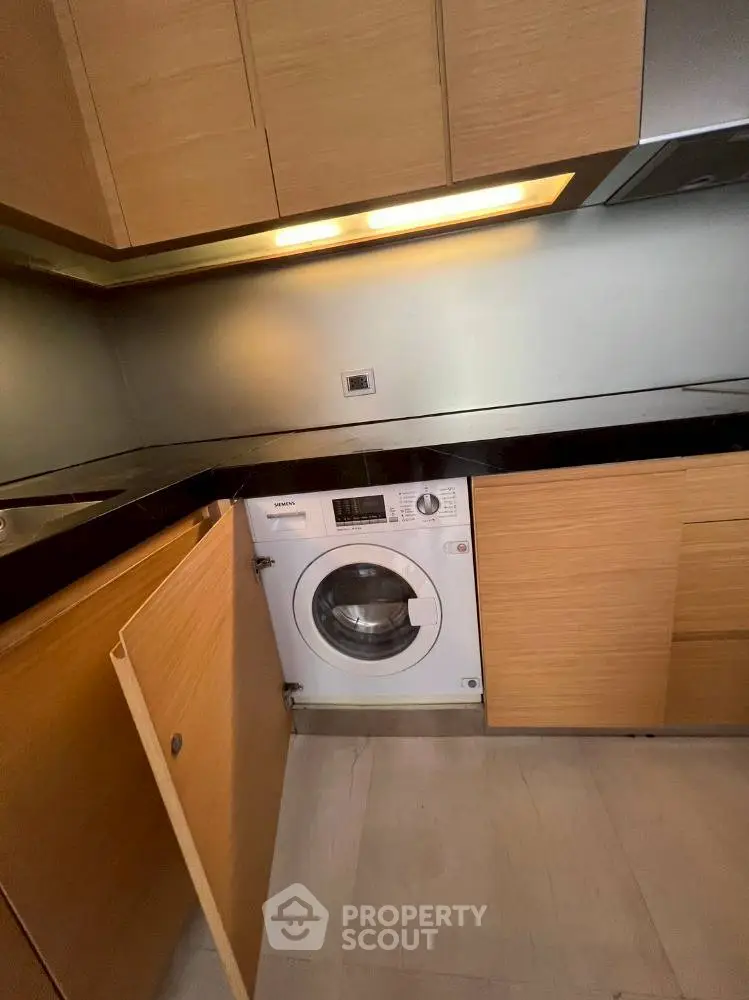 Modern kitchen with integrated washing machine and sleek wooden cabinetry.