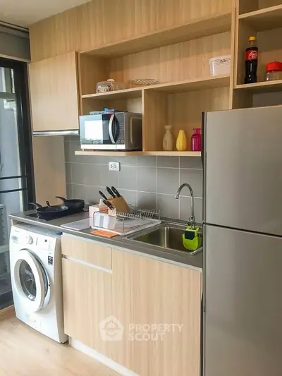 Modern kitchen with washing machine and stainless steel fridge in stylish apartment.