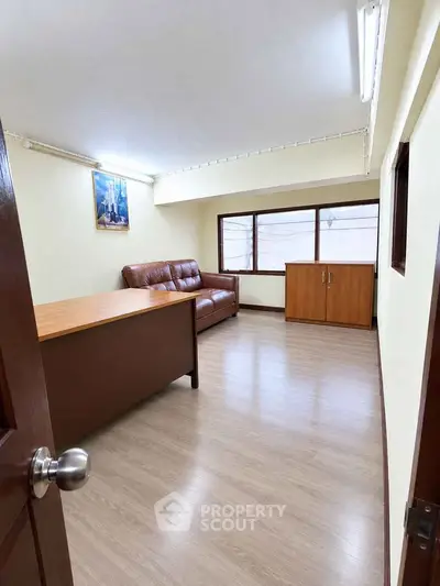 Spacious office room with wooden desk and leather sofa, ideal for professional work environment.