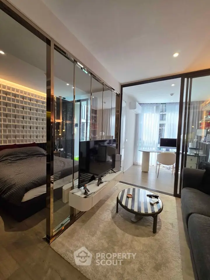 Modern apartment with open layout, featuring a cozy living room and stylish bedroom separated by glass doors.