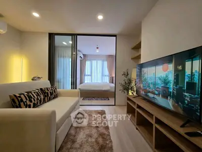 Modern living room with cozy sofa and large TV, open view to bedroom