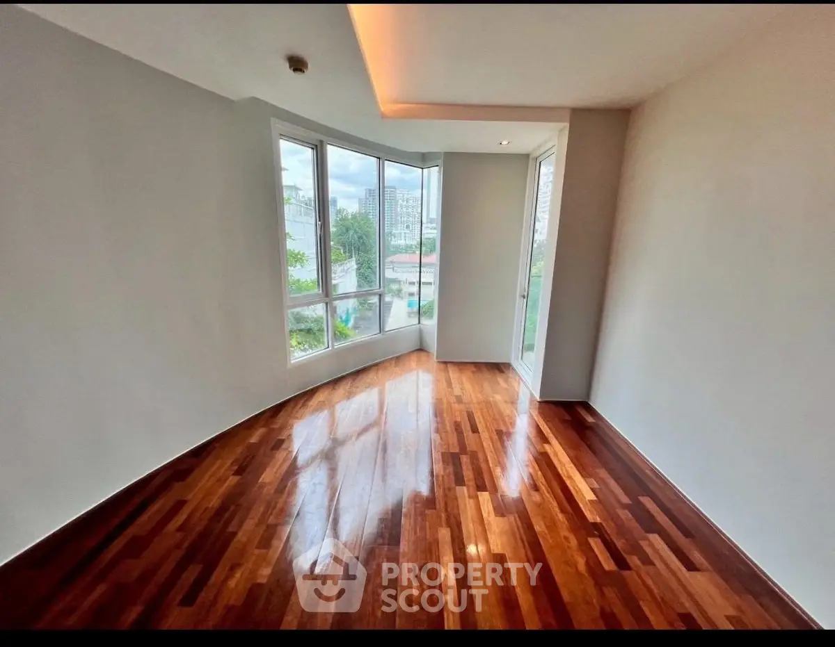 Spacious room with hardwood floors and large windows offering city views