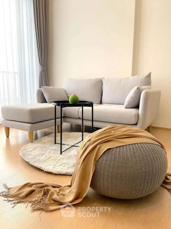 Modern living room with cozy sofa, stylish pouf, and elegant decor in bright natural light.