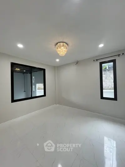 Spacious empty room with elegant chandelier and large windows, perfect for customization.