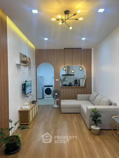 Modern living room with stylish lighting and cozy sofa, featuring a view into a compact kitchen area.