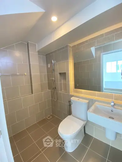 Modern bathroom with sleek fixtures and neutral tiles, featuring a shower and toilet.