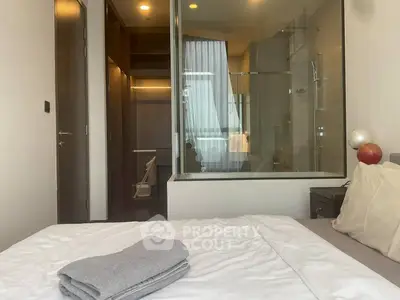 Modern bedroom with glass-walled bathroom and cozy bedding, offering a sleek and contemporary design.