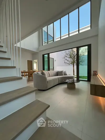 Spacious modern living room with high ceilings and large windows overlooking a serene garden.