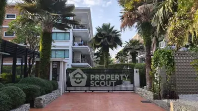 Luxurious gated entrance to modern apartment complex with lush landscaping and palm trees.