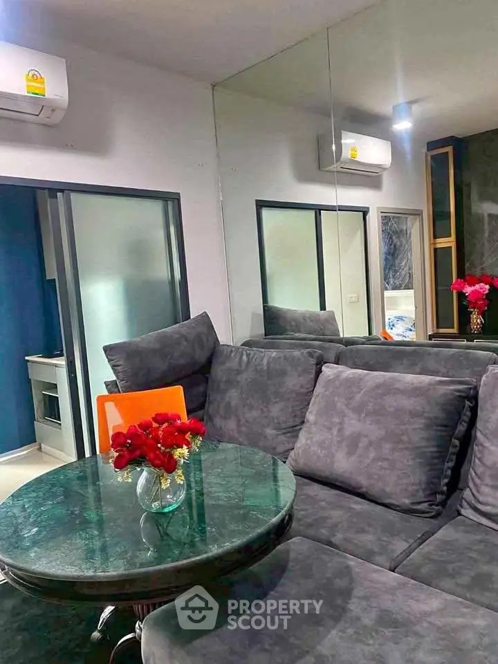 Modern living room with plush gray sofa and glass table, accented by vibrant red flowers, reflecting a cozy ambiance.