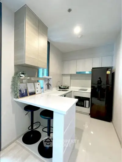 Modern kitchen with sleek design, featuring black fridge and bar stools, ideal for urban living.