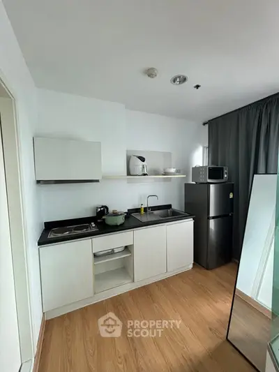 Modern compact kitchen with sleek appliances and wooden flooring in a stylish apartment.