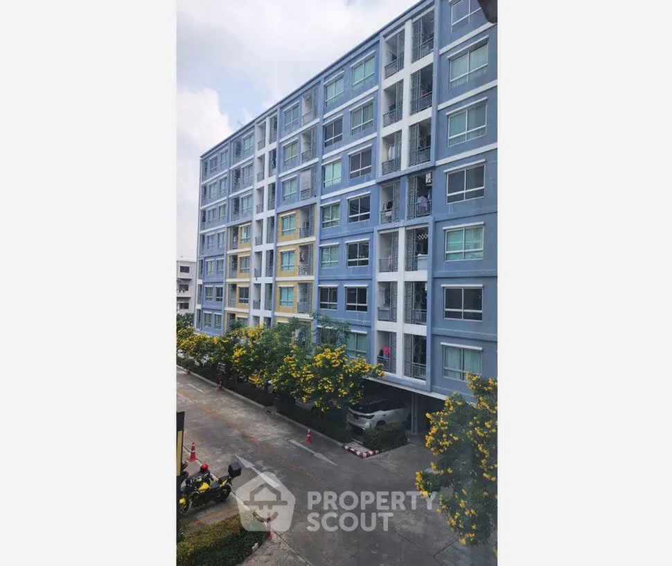 Modern blue apartment building with lush landscaping and ample parking space.