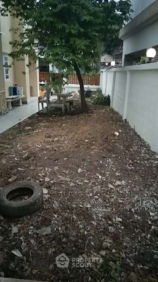 Spacious garden area with potential for landscaping, featuring a tree and outdoor seating in a residential setting.