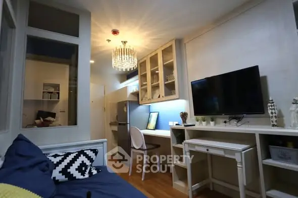 Modern living room with stylish decor and open kitchen layout, featuring a chandelier and flat-screen TV.