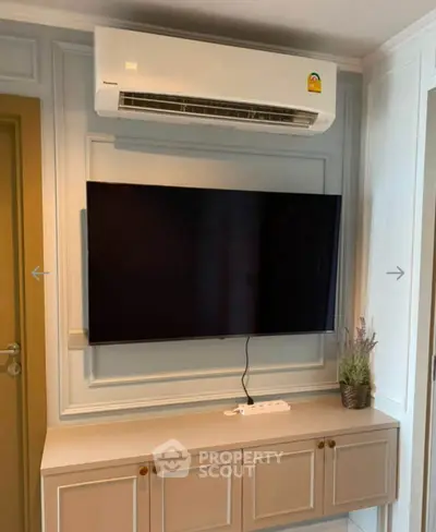 Modern living room with wall-mounted TV and air conditioner, stylish cabinetry below.