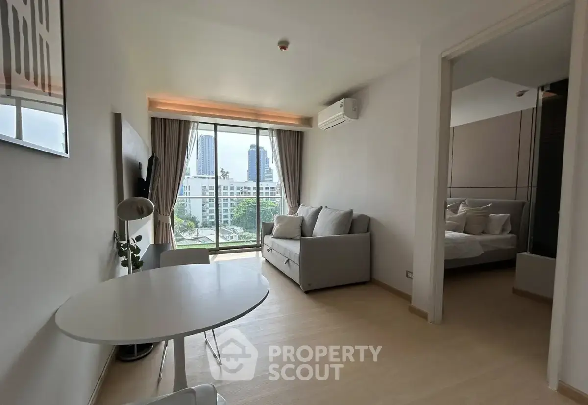 Modern living room with city view, featuring sleek furniture and natural light, adjacent to a cozy bedroom.