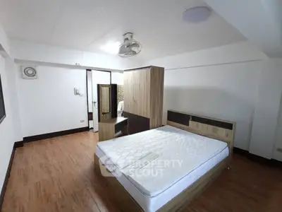 Spacious bedroom with wooden flooring and modern furniture in a well-lit apartment.
