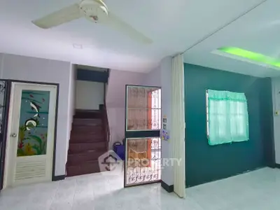 Spacious living room with unique wall art and ceiling fan, featuring a staircase and natural light.