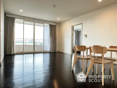 Spacious modern living room with wooden flooring and large windows leading to balcony.