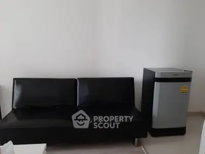Modern living room with sleek black sofa and compact fridge, perfect for urban living.