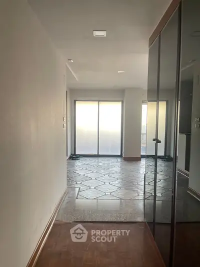 Spacious hallway leading to a bright living area with large windows and modern flooring.