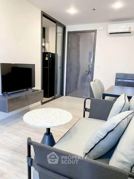 Modern living room with sleek furniture and open layout, featuring a wall-mounted TV and air conditioning.