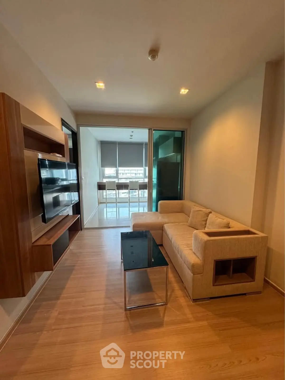 Modern living room with sleek wooden flooring and cozy sectional sofa, leading to a bright dining area.