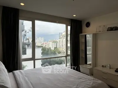 Spacious bedroom with large window offering stunning city views in modern apartment.