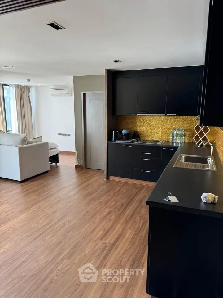Modern open-plan kitchen and living room with sleek black cabinets and wood flooring.