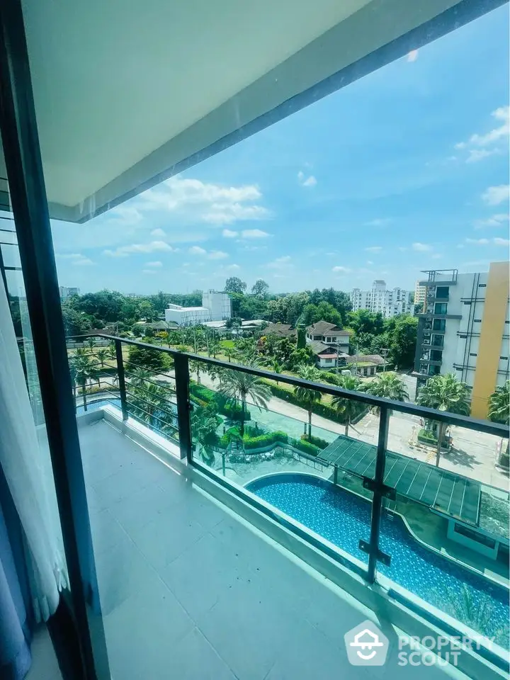 Stunning balcony view overlooking lush greenery and a sparkling pool in a modern apartment complex.